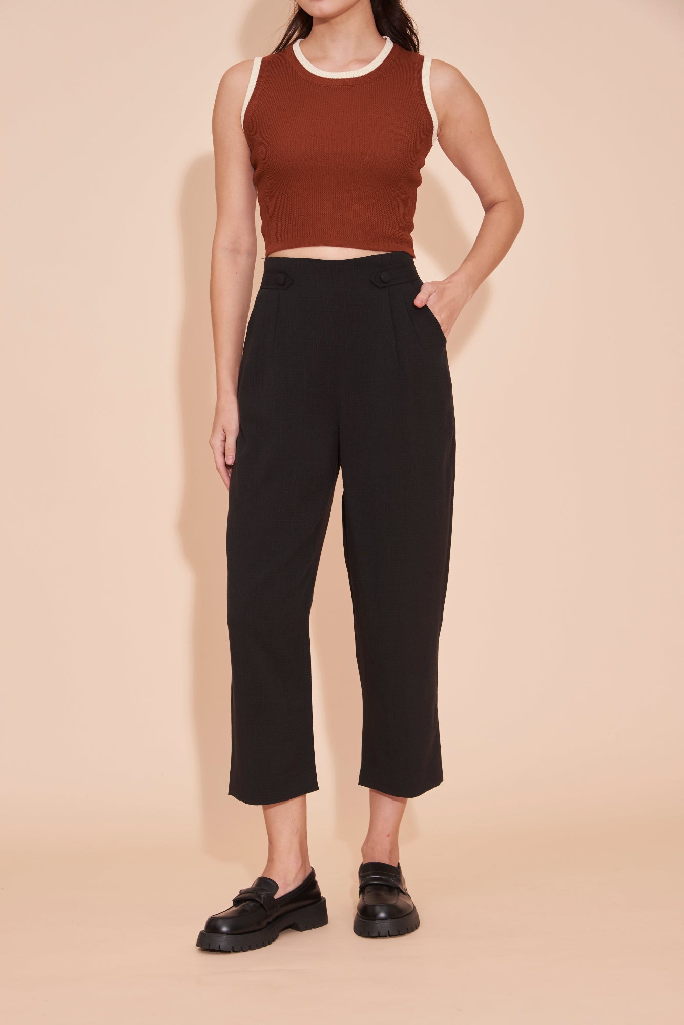 Person wearing a brown crop top and black pants on a beige background