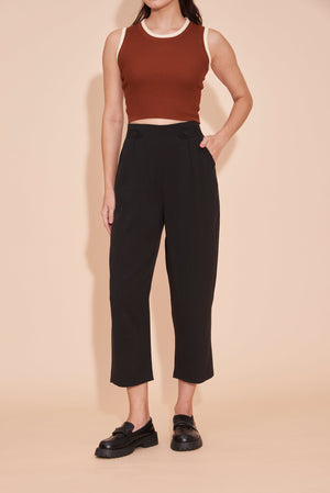Person wearing a brown crop top and black pants on a beige background